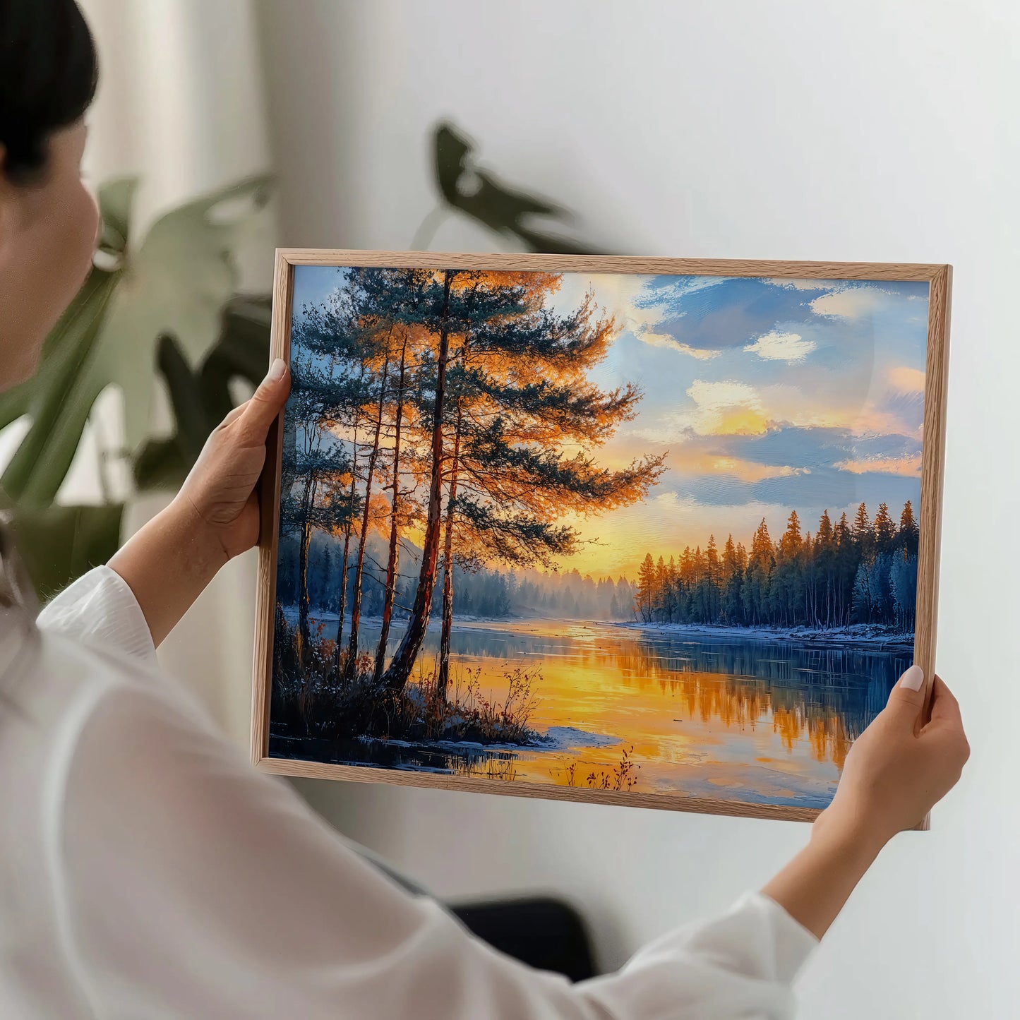 Person holding a framed painting of a sunset over a lake with trees.