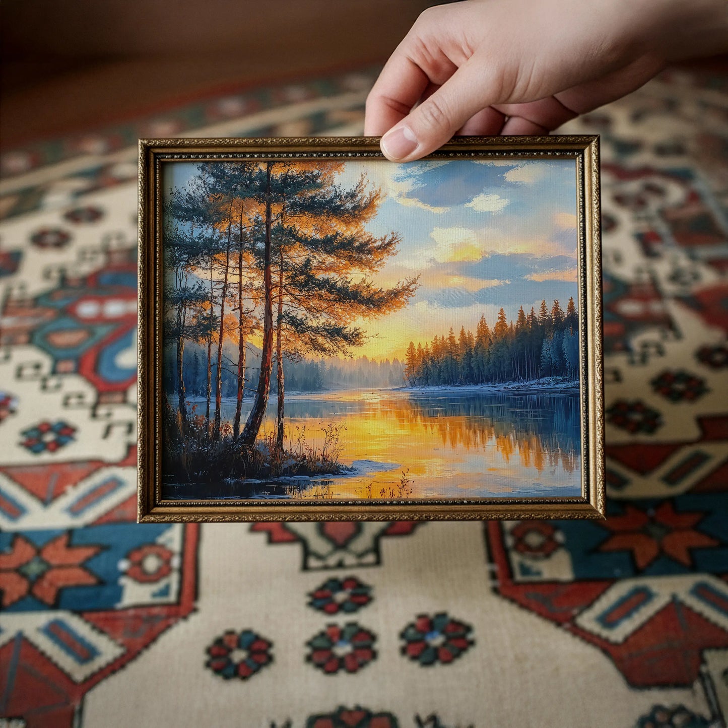 Close view of hands holding a horizontal canvas print, showing a forest river at sunset with glowing reflections.