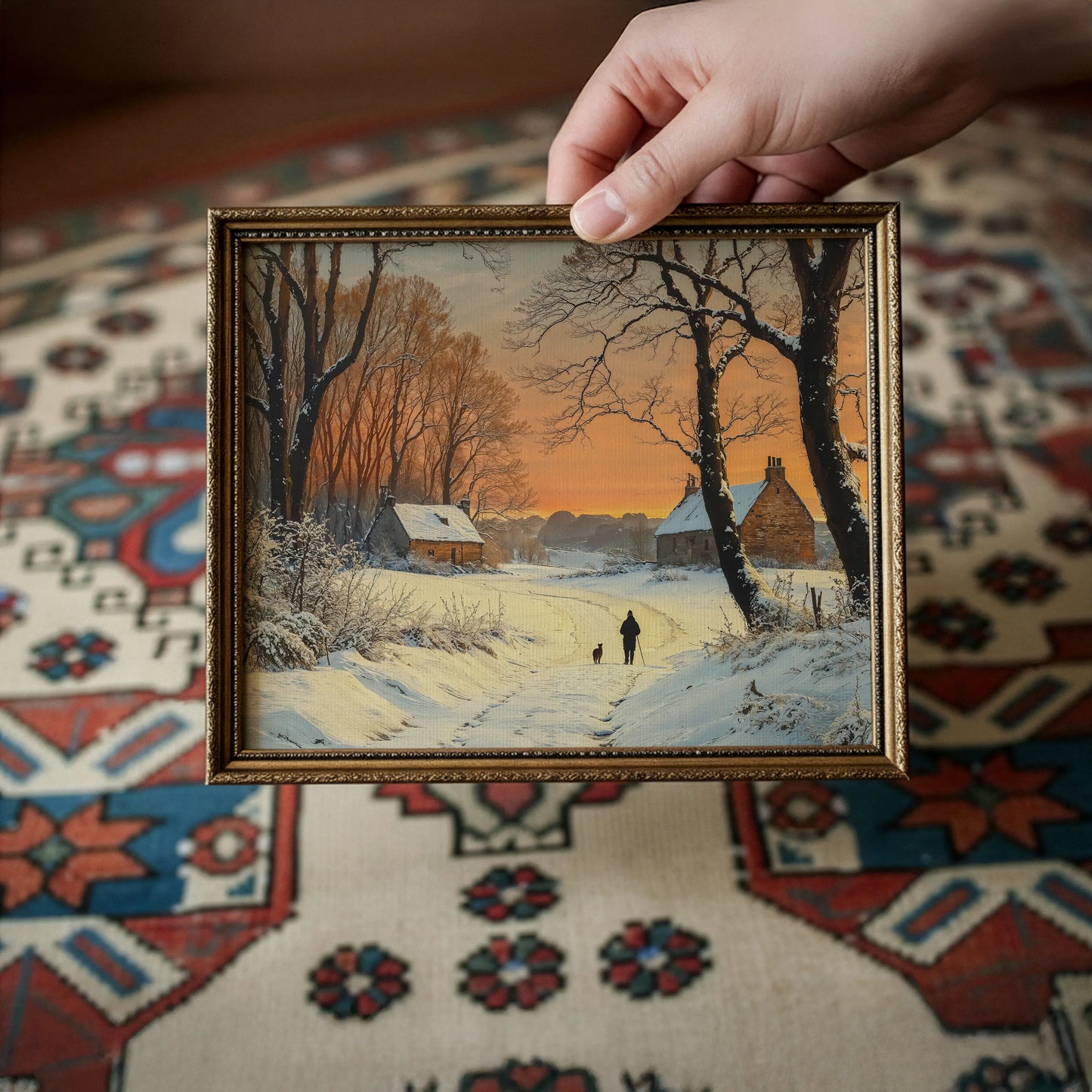 Framed winter landscape painting held by a hand on a patterned rug