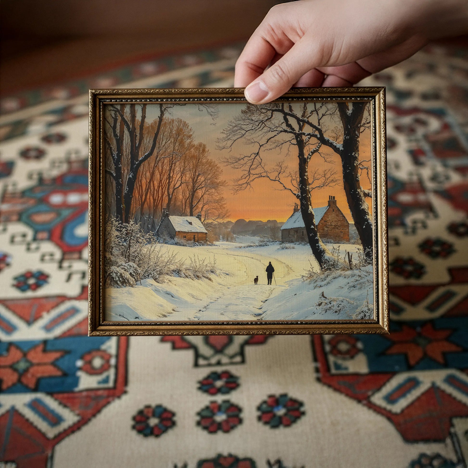 Framed winter landscape painting held by a hand on a patterned rug