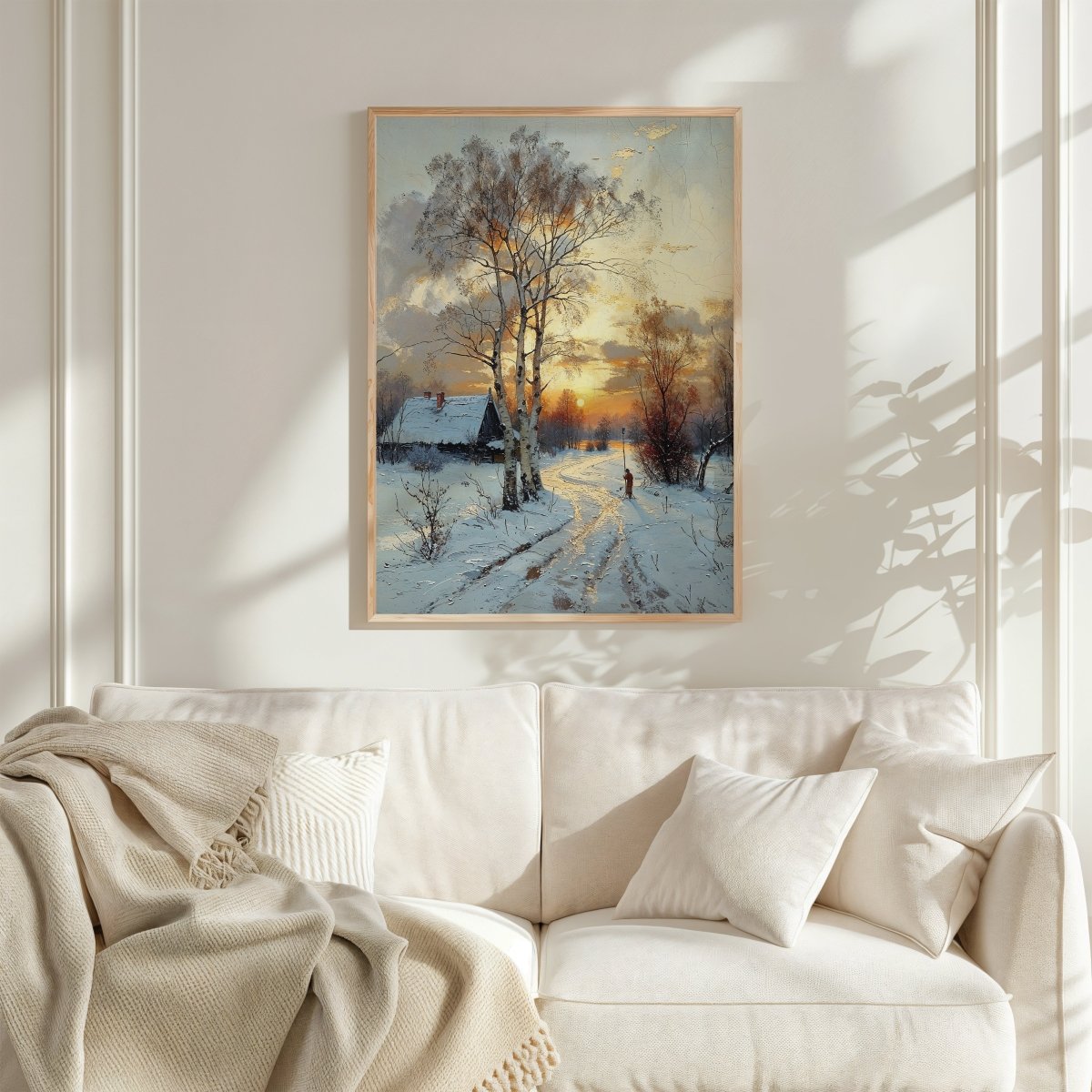 Framed winter landscape painting above a white sofa in a bright room.